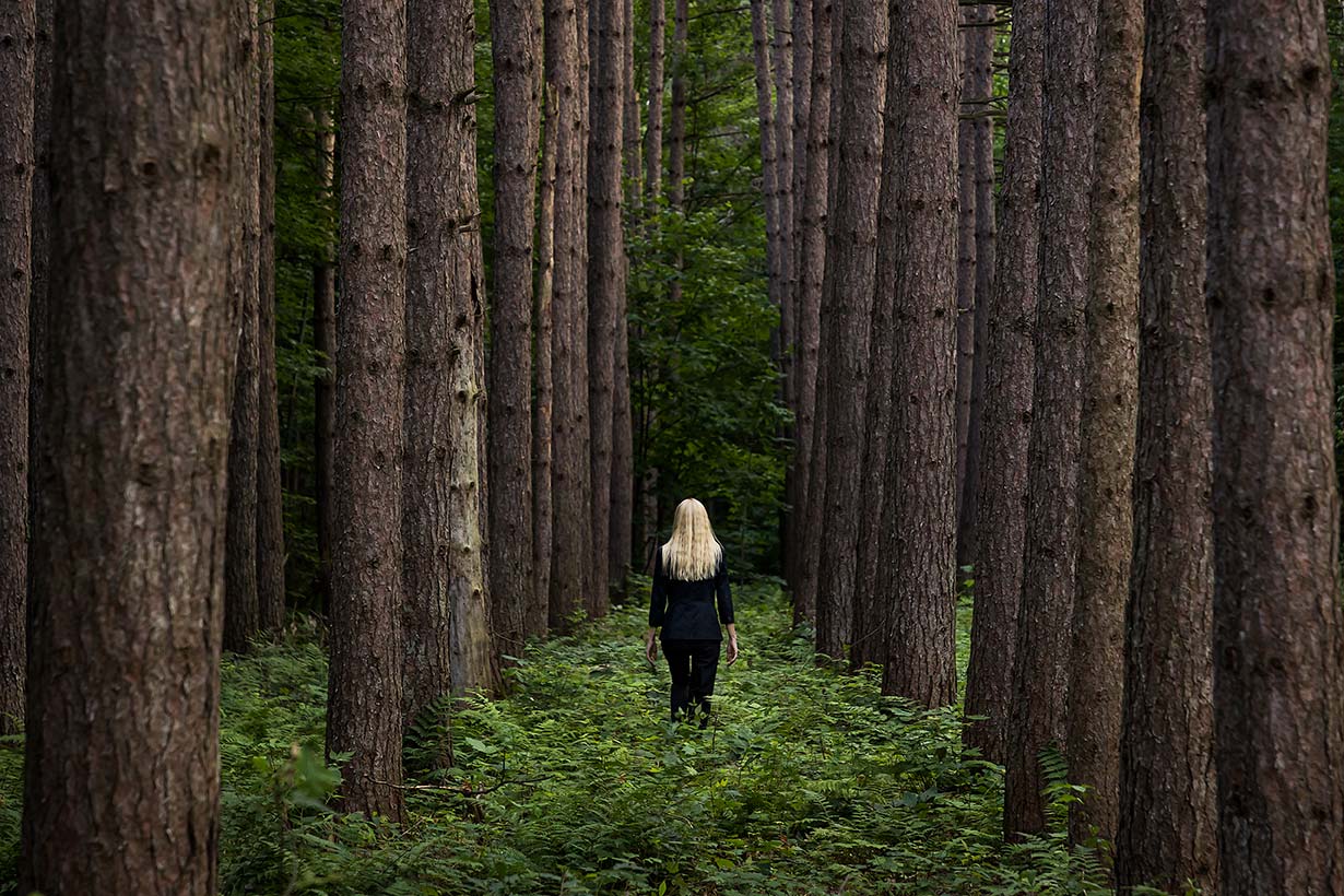 Le Repos de la Guerrière - Behind Me - Woman walking between towering pine trees.