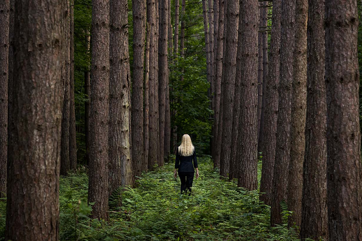 Le Repos de la Guerrière - Derrière Moi - Woman walking between towering pine trees.