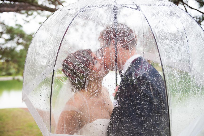 Photo of bride and groom under an umbrella in the rain by Marili Clark Photographer.