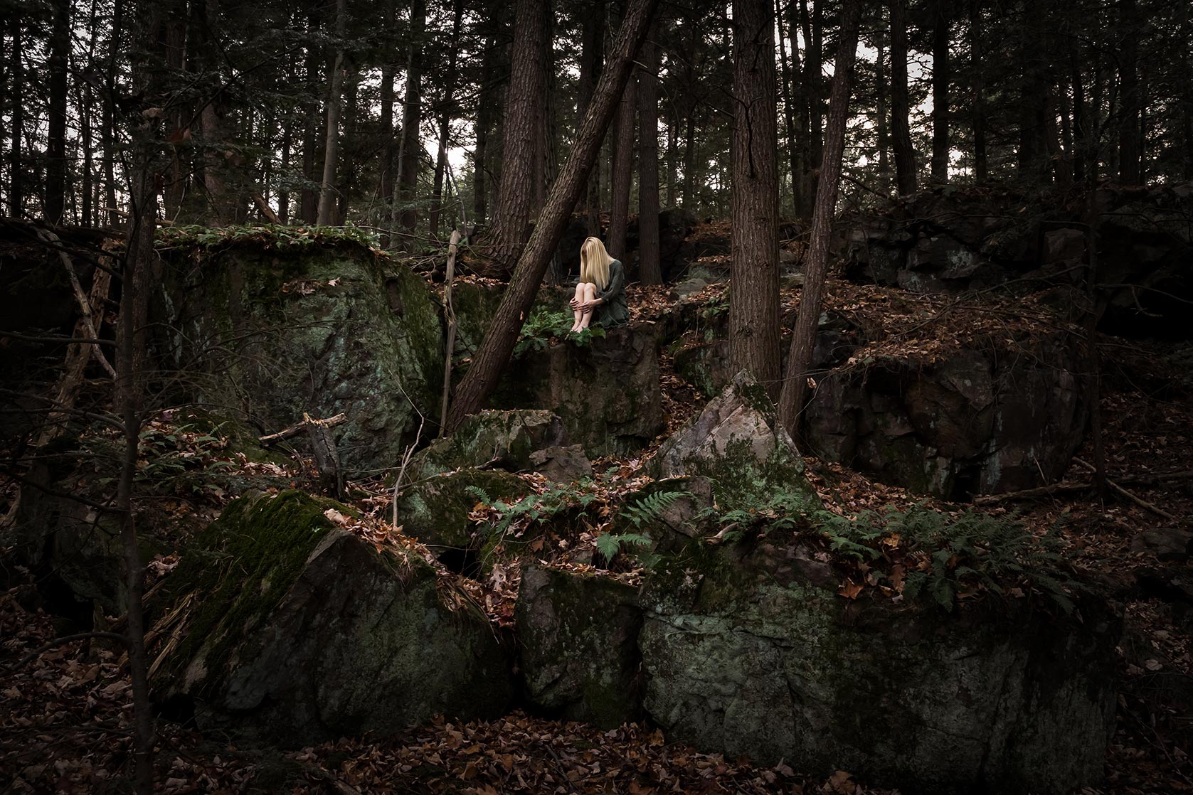 Le Repos de la Guerrière - Solitude - Woman in green dress sitting in a lush forest on a large rock.