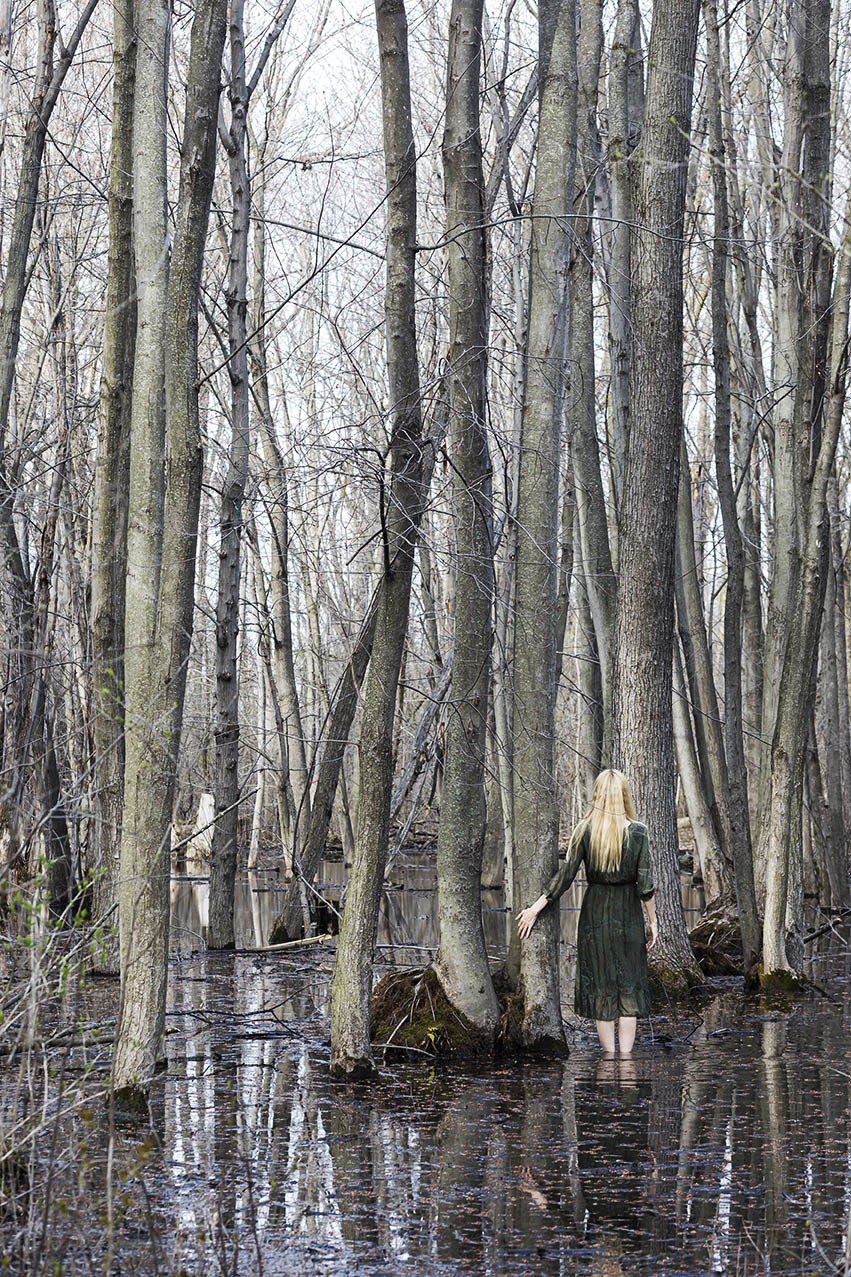 Le Repos de la Guerrière - Among Friends - Woman in green dress standing in a swamp with her outstretched hand touching a tree.