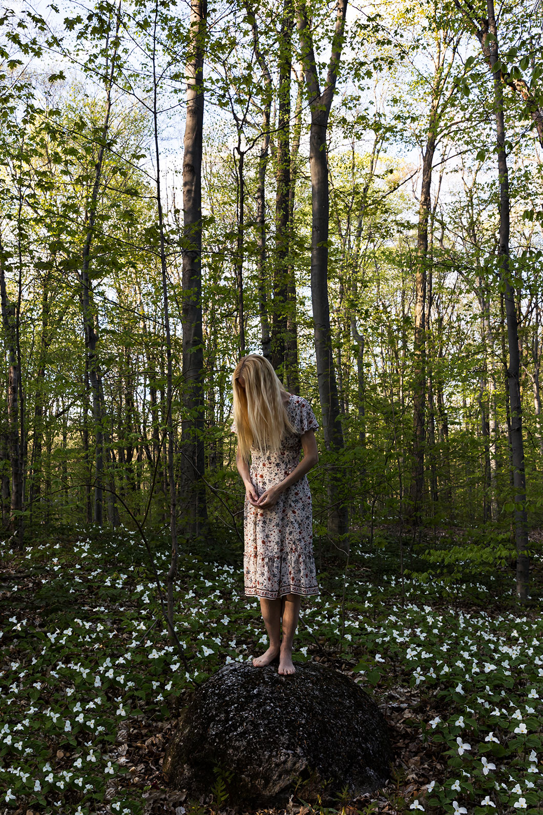 Le Repos de la Guerrière - Humble - Woman in flower dress standing on a rock surrounded by great white trillium flowers.